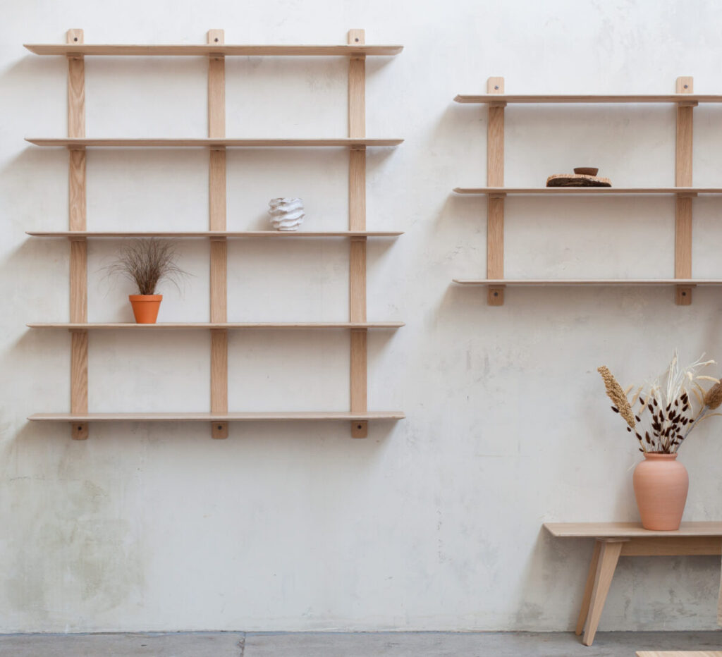 Two exposed wall shelving units with oak veneer finish and in multiple tiers with plants and ornaments sat on the shelf