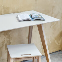 An open book sits atop a Brenin Desk Table with a mushroom coloured linoleum surface. It's simple elegant design make it a practical and elegant workspace.